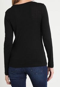 Zwarte longsleeve top met een ronde halslijn, gemaakt van lichtgewicht stof. Heeft een aansluitend ontwerp en is gecombineerd met spijkerjeans.