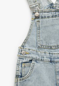 Denim overalls i lyseblå med justerbare skulderstropper. Har sølv hardware, forlommer og gule søm-detaljer.