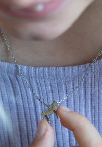 Zilveren ketting met een kleine, gedetailleerde paardenhanger. Hanger is van metaal met een gladde afwerking. Gekleed met een lavendel ribbeltop.