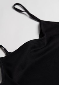 Schwarzes Cami-Top mit dünnen Trägern, aus einem glatten, dehnbaren Stoff. Verfügt über einen weichen, abgerundeten Ausschnitt und minimale Nähte.