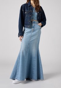Veste en jean de couleur foncée, portée sur une jupe en jean bleu clair avec un ourlet évasé. Les deux vêtements présentent des coutures classiques et des boutons.