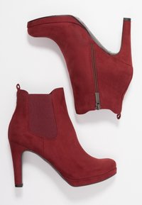 Red suede ankle boots with a high heel, featuring elastic side panels, a back zipper, and a smooth, textured finish.