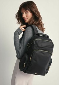 Czarny plecak z nylonu z złotymi suwakami, wieloma kieszeniami, górną rączką oraz wyściełanymi szelkami dla komfortu. Charakteryzuje się eleganckim, minimalistycznym designem.