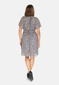 Kurzärmliges, knielanges Kleid mit dunkelblauem Grund, floralem Muster in Gelb und Weiß, elastischem Taillenbund und einem Bindeband am Rücken. Trägt man mit schwarzen Absätzen.