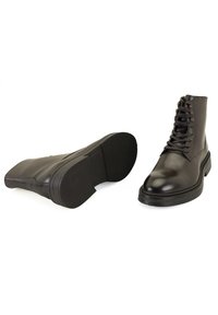 Bottes basses en cuir noir avec un bout arrondi, un laçage à l'avant et une semelle en caoutchouc texturée. Comprend des œillets en métal et une finition lisse.