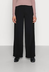 Zwarte wijde broek met een gladde textuur, voorzien van plooien aan de voorkant en een hoge taille, gecombineerd met een lichtroze aansluitend sweater.