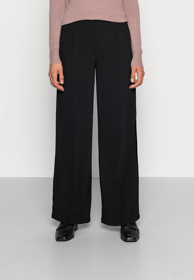 Zwarte wijde broek met een gladde textuur, voorzien van plooien aan de voorkant en een hoge taille, gecombineerd met een lichtroze aansluitend sweater.