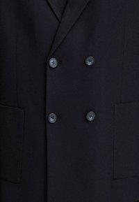 Nahaufnahme eines schwarzen, doppelreihigen Blazers mit vier schwarzen Knöpfen und zwei aufgesetzten Taschen auf der Vorderseite.
