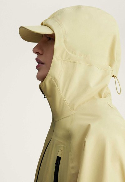 Chaqueta impermeable de color amarillo claro con capucha, que cuenta con un cierre de cremallera y una visera para mayor protección. Textura lisa y diseño ergonómico.