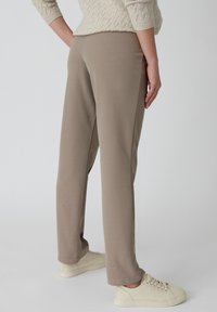 Beige sweatpants met een gladde textuur, slim fit en een elastische tailleband, gecombineerd met lichtgekleurde sneakers. De achteraanzicht toont de naaddetails.