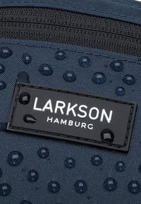 Tessuto blu con accenti circolari in rilievo, superficie testurizzata e un'etichetta nera con la scritta "LARKSON HAMBURG" in lettere bianche.