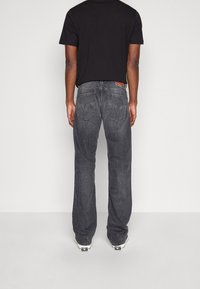 Černé tričko nošené se šedými džíny rovného střihu s kapsami na zádech zdobenými prošíváním. Textura působí jako džínovina. Přednesena je ležérní obuv.