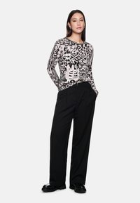 Long-sleeve black and white printed top with abstract patterns, paired with high-waisted black trousers and chunky black shoes.