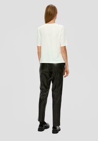 T-shirt blanc à manches courtes et pantalon en cuir noir ajusté. La tenue présente une coupe décontractée avec une texture douce et un design minimaliste.