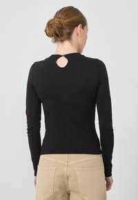 Svart langermet topp med rund hals og en liten nøkkelhullskjæring bak, kombinert med lyse beige bukser med baklommer.