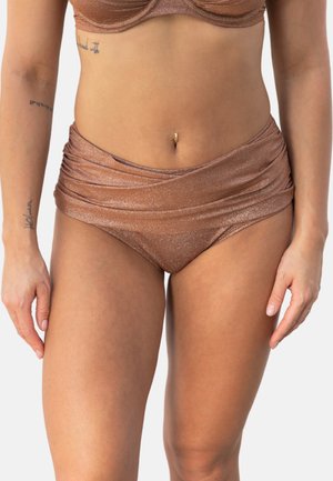 Frau trägt metallisch bronzefarbene, hoch taillierte Bikinihose und passendes Bikinioberteil, zeigt Tattoos an den Armen und einen Bauchnabelpiercing.