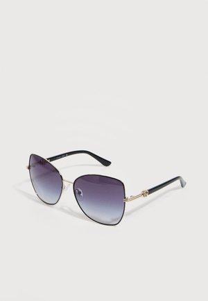 Gafas de sol estilo ojo de gato con montura negra y dorada y lentes degradadas en tonos morado oscuro, que descansan sobre una superficie blanca.
