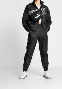 Svart vindjacka med vit märkning, kombinerad med svarta joggerbyxor. Vita sneakers med svarta och grå accenter.