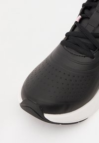 Černá sportovní bota s texturovaným povrchem a malými perforacemi, plochými tkaničkami a bílým akcentem ve střední části. Zaoblený design špičky.