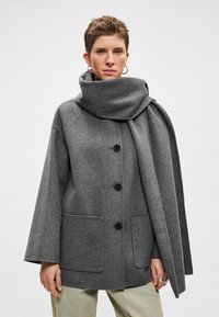 Hall villane mantel laia varruka, nööpide sulgemise ja kahe ees taskuga. Omab suurt voltis salli, mis langeb kaela ümber.