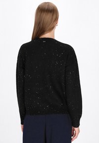 Sort strikket sweater med en løs pasform, der har metalliske prikker over det hele. Ribbestrikkede manchetter og kant giver struktur til designet.