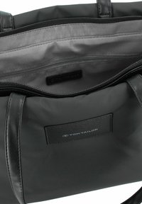 Zwarte draagtas met leren accenten, ritsopening en grijze stofvoering. Het interieur heeft een ritsvak en een merklabel.