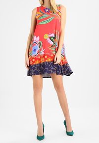 Barevné šaty bez rukávů s květinovými vzory; červený vršek a tmavě modrá sukně s květinovými motivy. Materiál vypadá hladký a lehký.