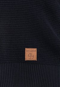 Ciemnoniebieski sweter o fakturowej strukturze, z prążkowanym dołem i taninową skórzaną metką z wyszywanym logo "KEY LARGO" z przodu.