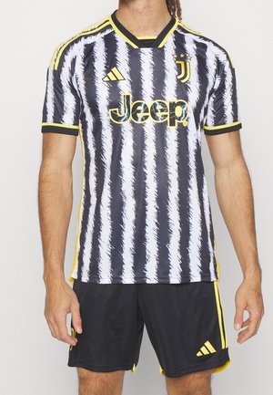 Maglietta da calcio a righe bianche e nere con accenti gialli, caratterizzata da un colletto a V e il logo "Jeep" sul davanti, abbinata a pantaloni corti neri.