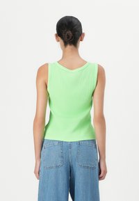 Top de tirantes verde acanalado con escote redondeado, combinado con jeans de pierna ancha en azul claro que cuentan con dos bolsillos traseros.