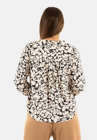 Blusa de manga larga beige claro con un patrón floral negro, fabricada con un tejido texturizado y detalles plisados en la parte posterior para añadir dimensión.