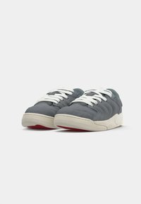 Baskets en daim gris avec des lacets blancs, dessus texturé, bout rond et semelle intermédiaire couleur crème avec un accent rouge sous la semelle.