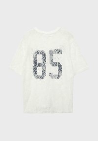 Haut à manches courtes en dentelle blanche avec un grand chiffre "85" en dentelle noire imprimé sur le devant.