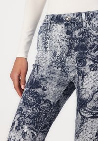 Blomster-mønstrede denimjeans i marineblå og lysegrå, med en tettsittende design og subtil tekstur. Metallknapplukking i livet.