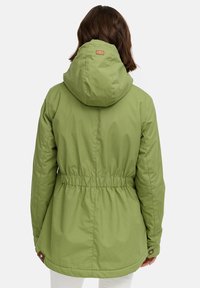 Knee-length grön jacka med åtstramad midja, mjuk textur, huva och en rektangulär logotyp-patch på ryggen. Knappar vid ärmarna.