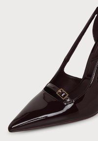 Chaussure à talon haut en cuir verni bordeaux foncé avec bout pointu, bride fine et petit détail de boucle dorée.