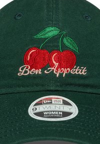 Groene baseballpet met geborduurde rode kersen en de tekst "Bon Appétit" in het roze. Voorzien van een verstelbare band en een "New Era" label.