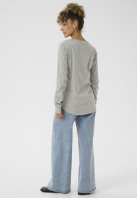 Grå langærmet skjorte med rundet kant, parret med lyseblå vidde jeans, begge lavet af blødt stof. Sorte fodtøj er også synligt.