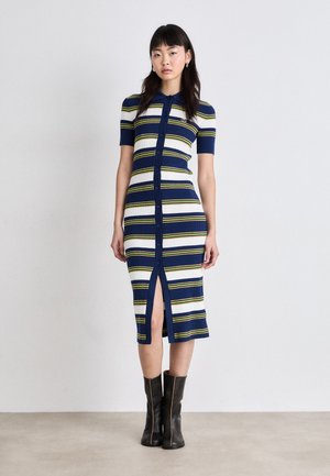 Knitted, striped dress featuring navy, white, and yellow colors; short sleeves, button closure, and front slit. Paired with black boots.