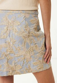 Jupe bleu clair avec broderies florales texturées en or et beige. Le design présente une coupe ajustée et une finition lisse.