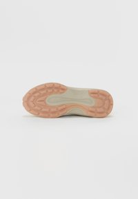 Beige sneakerpohja, jossa on teksturoitu kumi, sisältää voimakasta vaimennusta ja vaaleanpunaisen ulkopohjan, suunniteltu tarjoamaan pitoa ja mukavuutta.