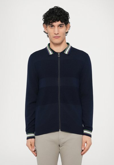 Navy zip-up cardigan with a striped collar featuring green, purple, and white. Textured horizontal bands and fitted cuffs.