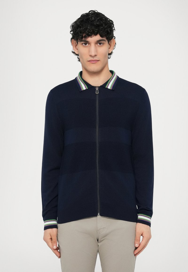 Námornícky modrý kardigán na zips s pruhovaným golierom v zelenej, fialovej a bielej farbe. Textúrované vodorovné pásy a priliehavé manžety.