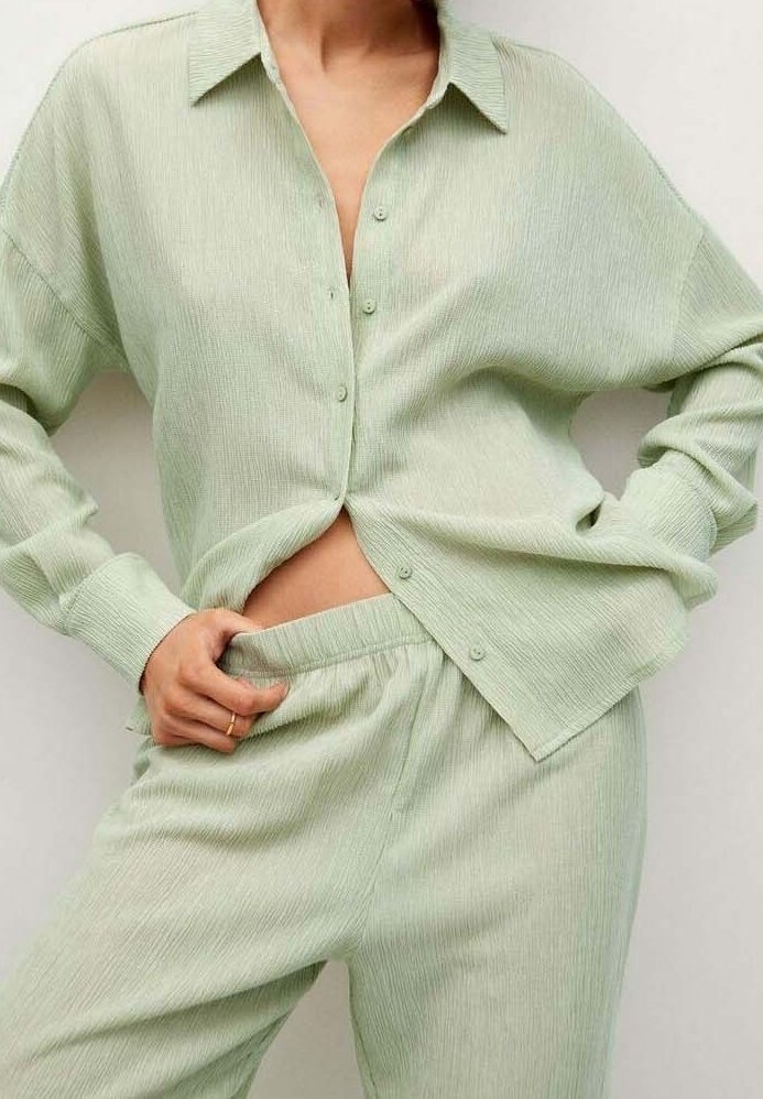 Personne portant une chemise boutonnée texturée vert clair et un pantalon assorti avec taille élastique, ajustant la taille du pantalon d’une main.