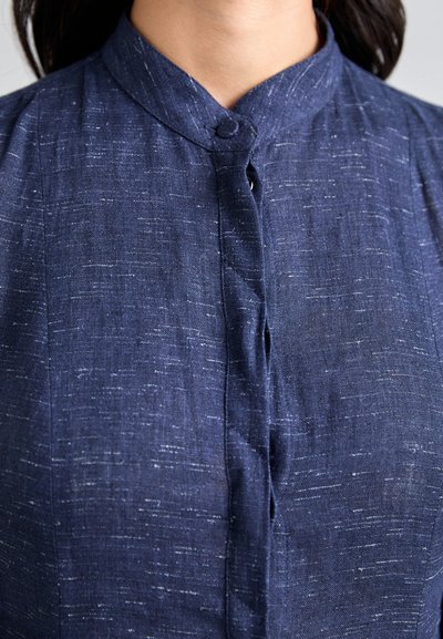 Navy blue linen blouse with a high collar and button-down front. Features subtle texture and slight sheen, with prominent stitching detail.