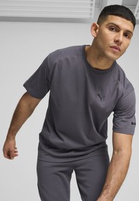 Grijs sportoutfit met een t-shirt met korte mouwen en een ronde halslijn, voorzien van een klein zwart logo. Glad materiaal en een relaxte pasvorm.