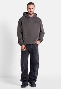 Grå hoodie av tjockt tyg med en framficka, ihop med svarta cargobyxor med sömdetaljer och fickor.