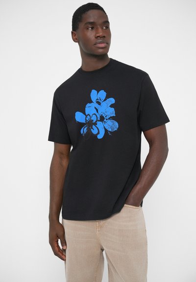 T-shirt en coton noir avec un motif floral bleu graphique sur le devant. Coupe décontractée avec manches courtes et col rond.