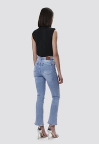 Top negro sin mangas combinado con jeans de tiro alto en azul claro. Los jeans tienen un corte recto y un parche de cuero marrón en la parte posterior.