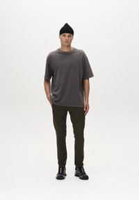 Camiseta de algodón gris de gran tamaño con mangas cortas y cuello redondo, combinada con pantalones oscuros verdes ajustados y zapatillas negras. Sombrero beanie negro como acento.